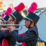 Olive Branch Mardi Gras Parade Adds Battle of the Bands High school marching band trumpet players in plumed hats performing in a parade, illustrating the Olive Branch Mardi Gras Battle of the Bands